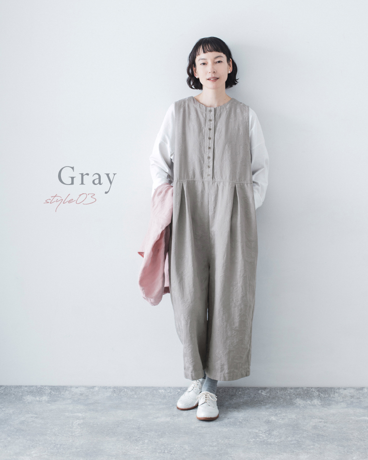 グレーの2wayオールインワンを白のロンTに重ね、ピンクの羽織りを手にした全身コーディネート画像