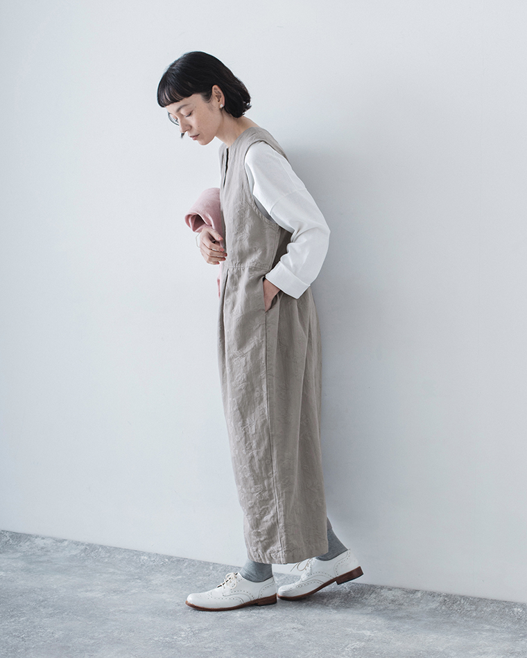 グレーの2wayオールインワンを白のロンTに重ね、ピンクの羽織りを手にした全身コーディネート画像