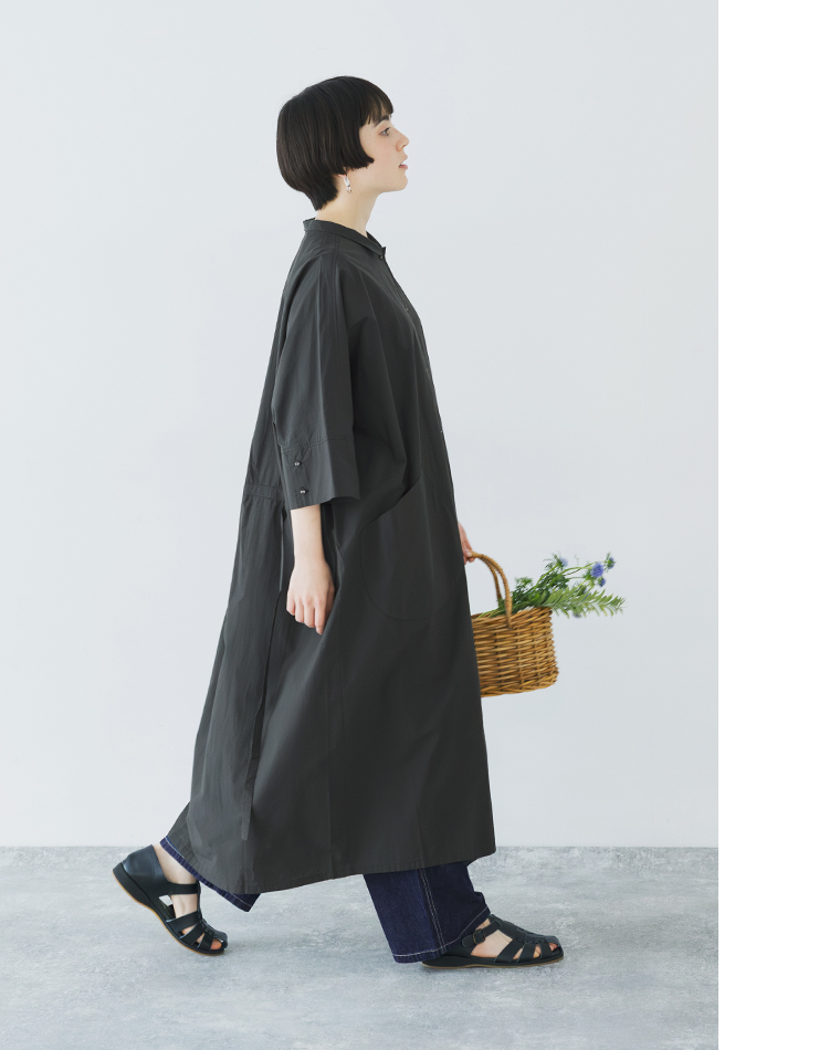 モスグレーのドルマンワンピースを着用した歩き姿のコーディネート（花の入ったバスケットを手にした横向きスタイル）