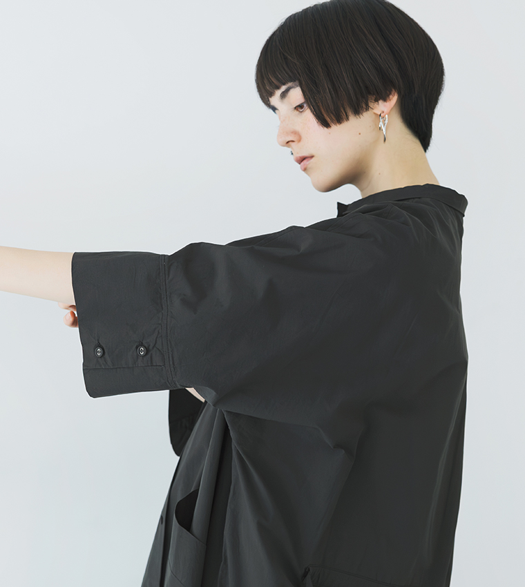 ブラックのドルマンワンピースを着用した横向きの上半身カット（腕を横に伸ばしたシルエットがわかる構図）