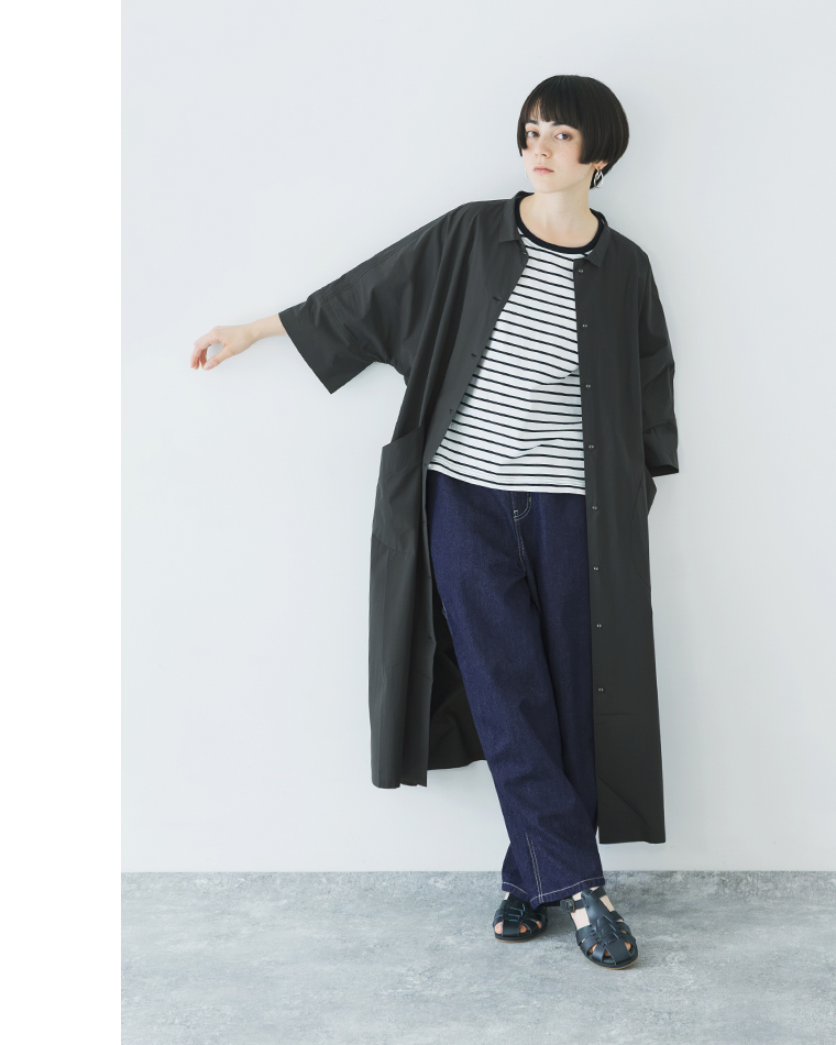 ブラックのドルマンワンピースを羽織ったコーディネート（ボーダーTとデニムを合わせ、片腕を横に伸ばした正面スタイル）