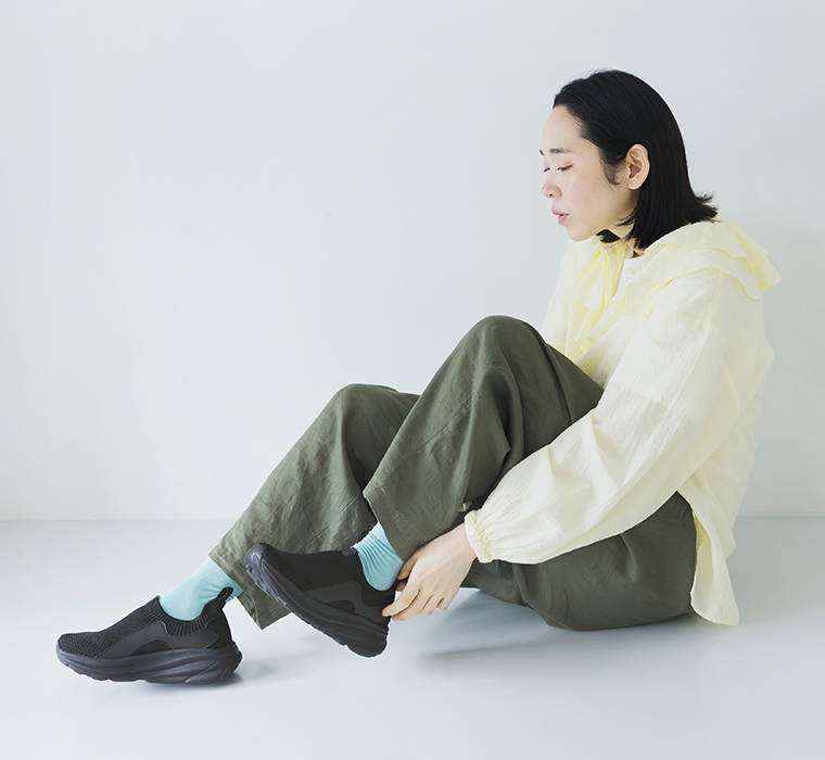 ブラックのニット編みスニーカーを着用して座るモデルの全身カット