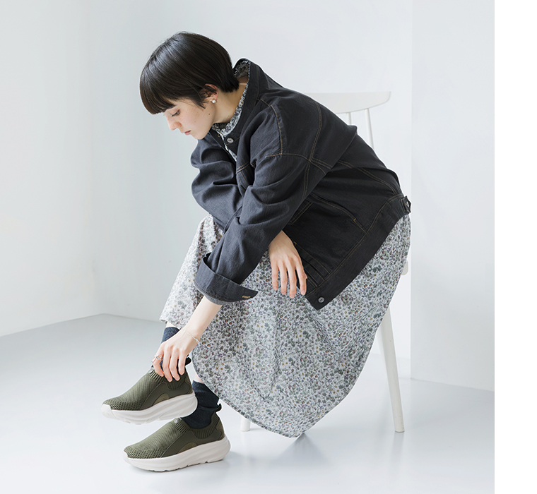 カーキのニット編みスニーカーを着用して座り、スニーカーを触るモデルの全身カット