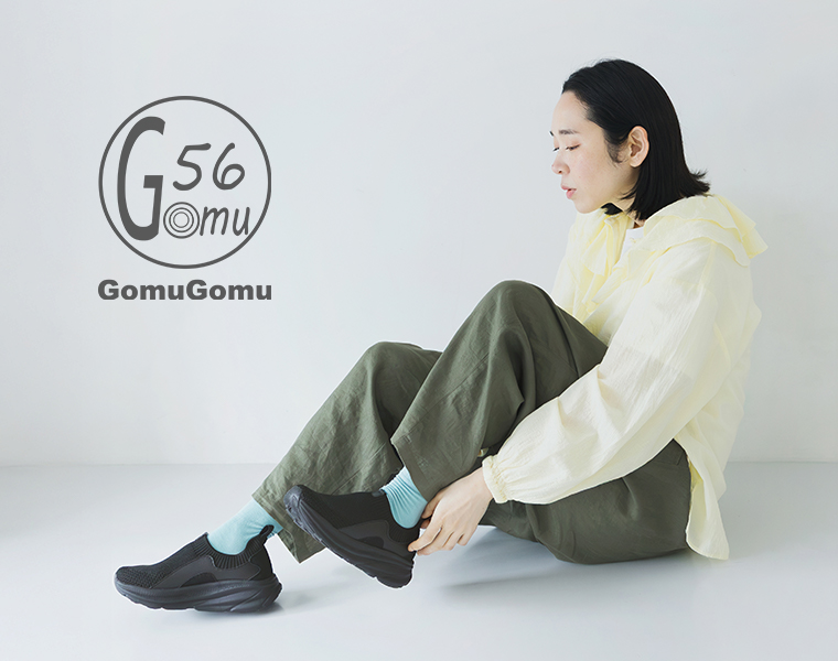 Gomu56のブラックのニット編みスニーカーを着用して座るモデルの全身カット