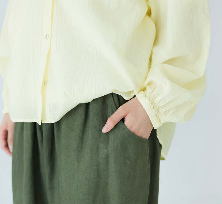 ライトイエローの長袖トップスをカーキのパンツにタックインし、右手をポケットに添えた上半身ディテールのコーディネート画像