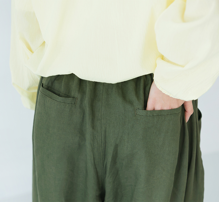 ライトイエローの長袖トップスにカーキのパンツを合わせ、右手をバックポケットに添えた後ろ姿のコーディネート画像