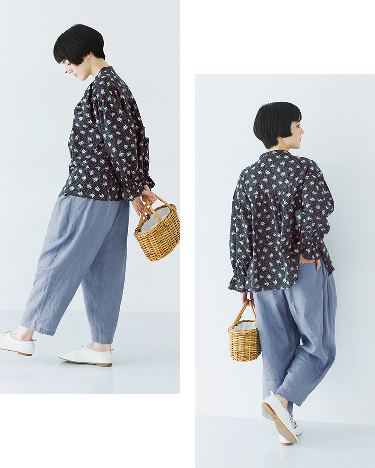 ネイビーの花柄トップスにブルーのパンツを合わせ、かごバッグを持って立つ全身コーディネート画像（2ポーズ比較）