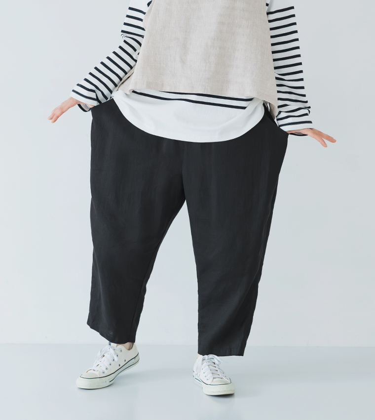 ボーダーの長袖トップスにベージュのベストを重ね、ブラックのパンツと白いスニーカーを合わせて立つ全身コーディネート画像