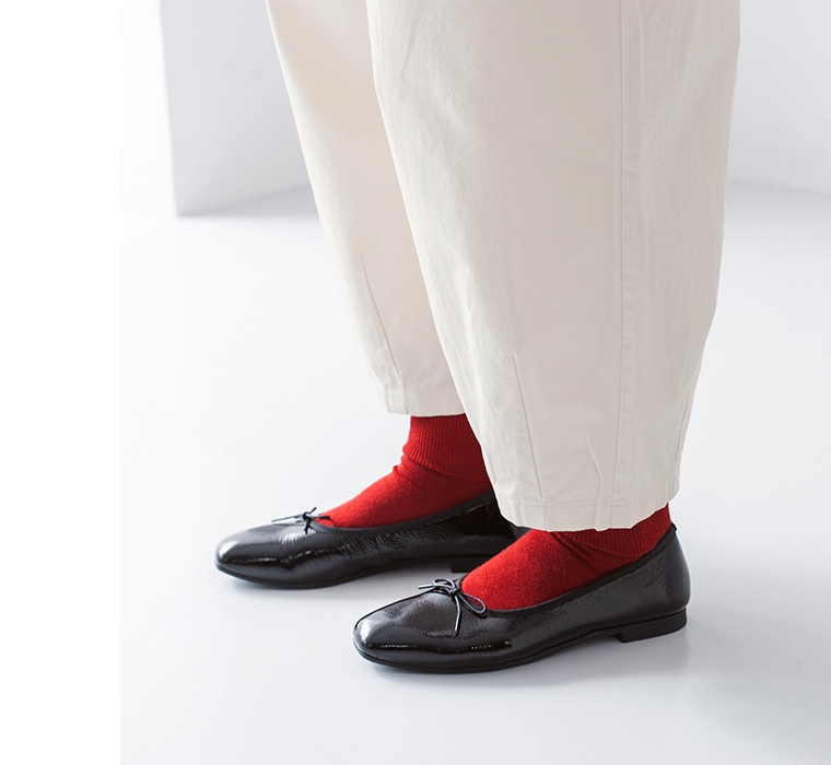 オフホワイトのパンツに赤い靴下と黒のバレエシューズを合わせた足元のコーディネートアップ