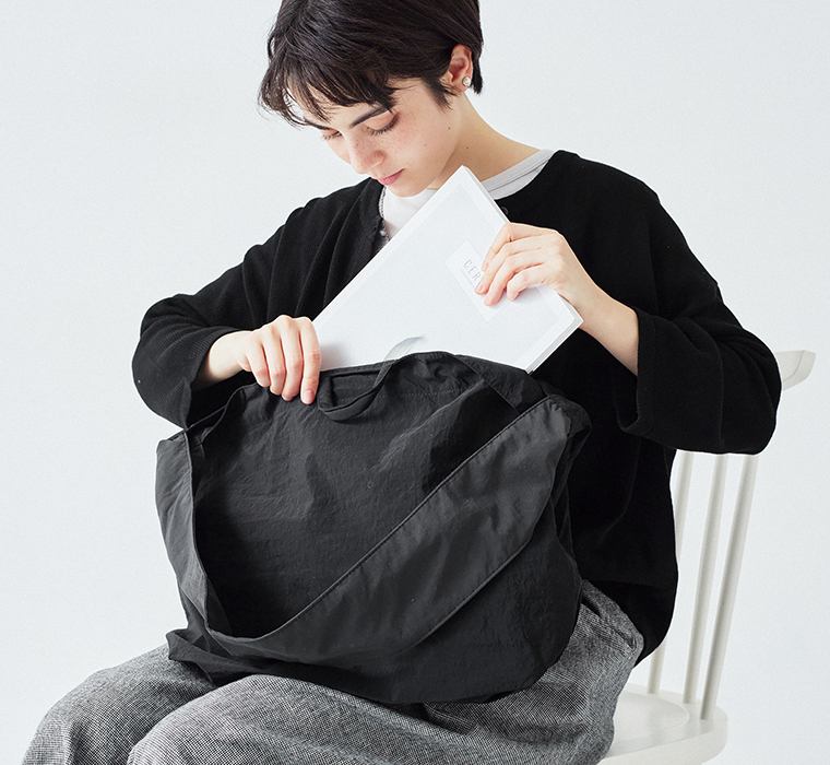 ナイロンリップストラップトートのブラックを肩に掛け書類を出し入れする様子