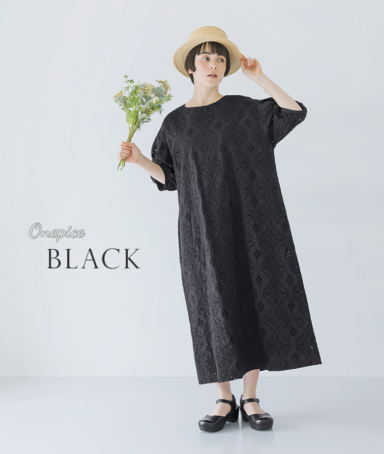 麦わら帽子をかぶったモデルがブラックのカットワークレースワンピースを着て花束を持ち正面を向いて立っている