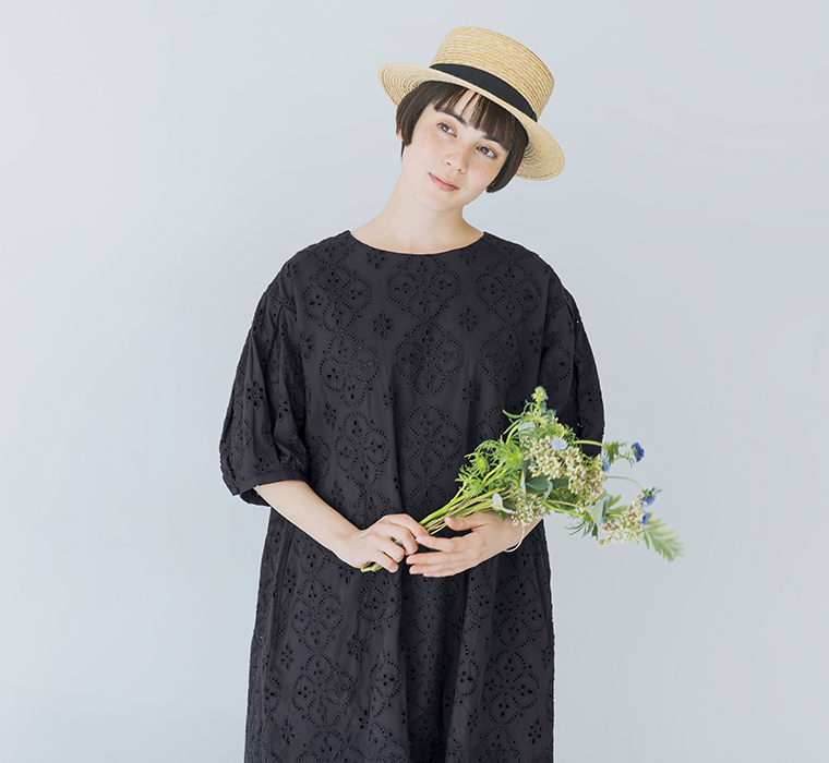 麦わら帽子をかぶったモデルがブラックのカットワークレースワンピースを着て花束を両手で持っている