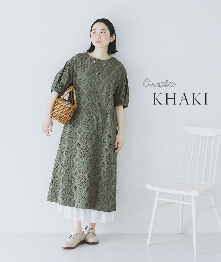 モデルがカーキのカットワークレースワンピースを着てかごバッグを持ち正面を向いて立っている