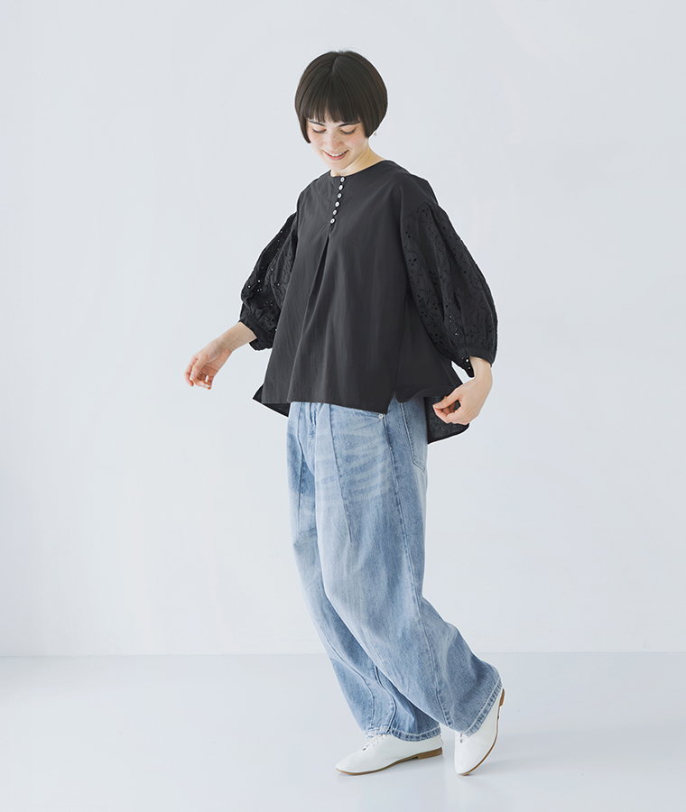 モデルがカットワークレーススリーブブラウスを着てデニムパンツと白いシューズを合わせて歩いている