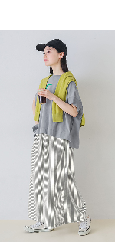 モデルがストライプフレアパンツを着てキャップとスニーカーを合わせドリンクを持って歩いている