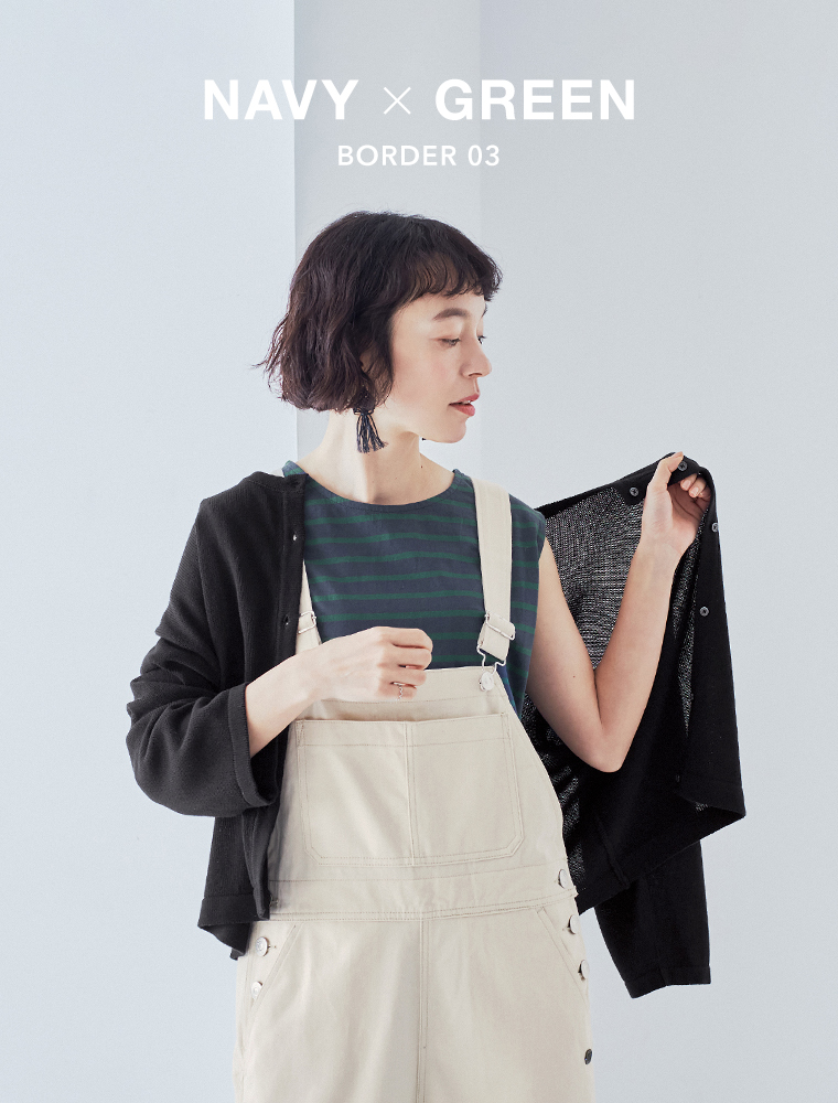 ネイビー×グリーンのボーダー柄トップスにライトベージュのオーバーオールを合わせ、黒の羽織りを片手に持った正面コーディネート画像