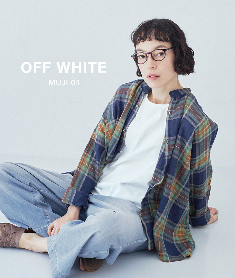 オフホワイトのタンクトップにマルチカラーのチェック柄シャツを羽織り、ライトブルーのワイドパンツとブラウンのサンダルを合わせて座っているコーディネート画像