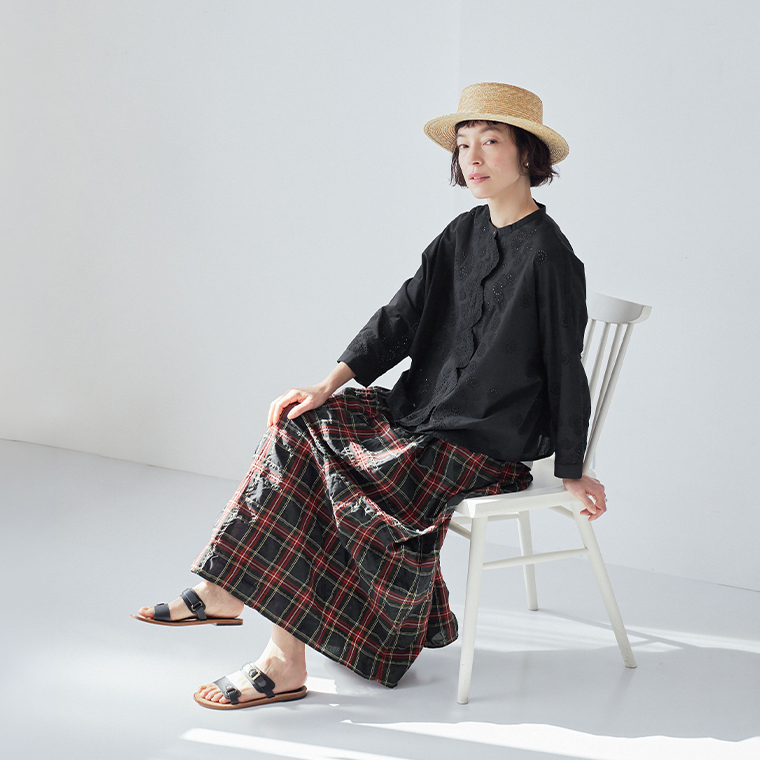 TUTIE. スカラップ刺繍レースブラウスのブラックを着た女性モデルの座り姿