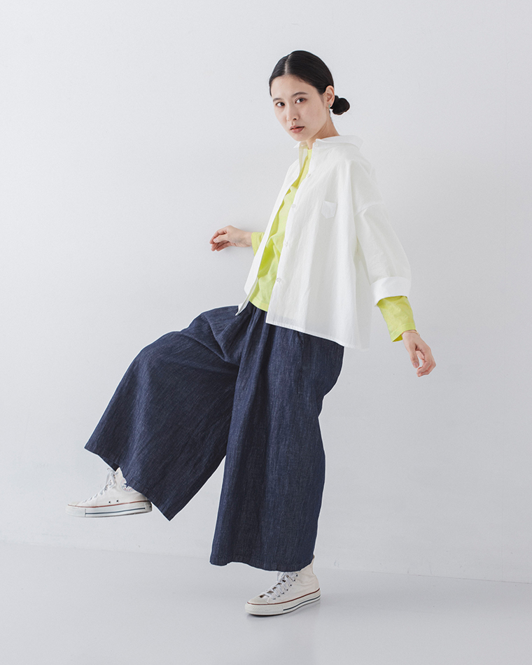 ホワイトのシャツにイエローのトップスとデニムパンツを合わせた人物が片脚を上げてポーズを取る着用コーディネート画像