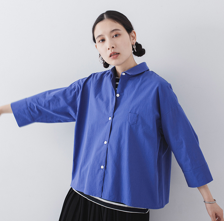 ブルーのシャツにボーダーインナーを重ねた人物が腕を伸ばして立つ着用コーディネート画像