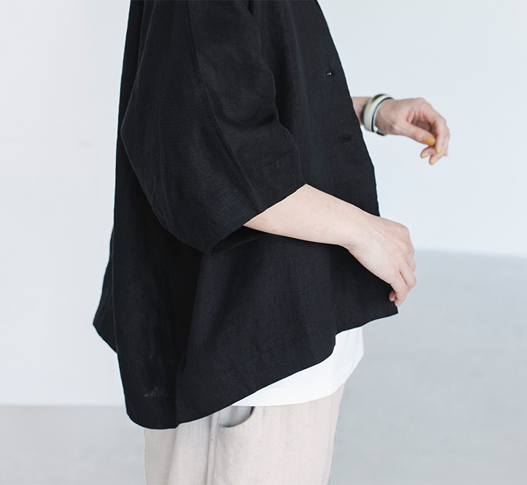 ブラックのリネンジャケットを白インナーとライトカラーのパンツに重ね、手元のしぐさを写した着用ディテール画像