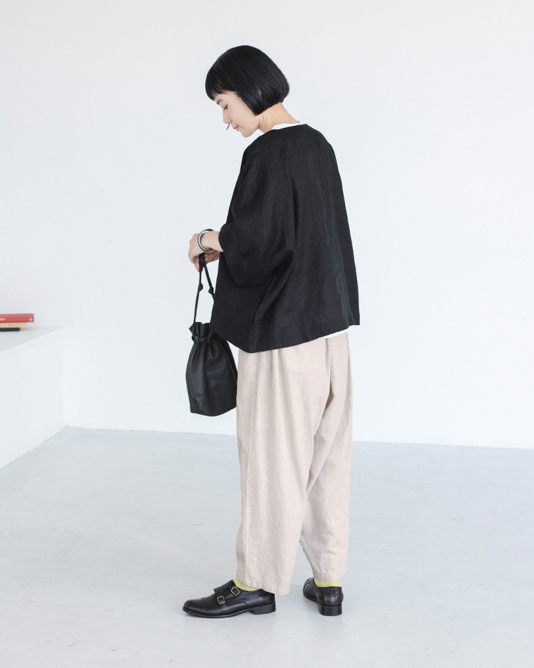 ブラックのリネンジャケットをライトベージュのワイドパンツに合わせ、小さな黒巾着バッグを持った着用コーディネート画像