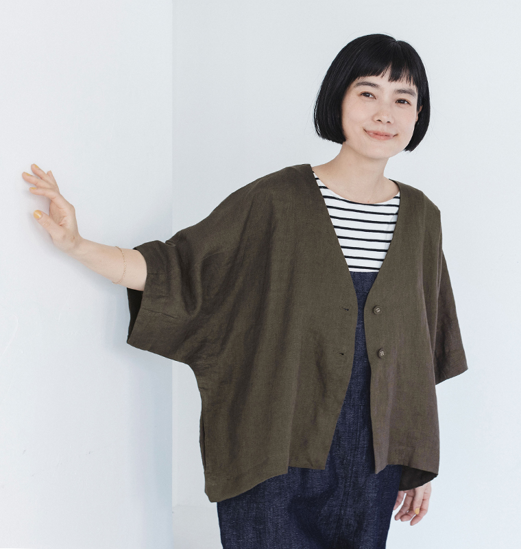カーキのリネンジャケットをボーダートップスとダークカラーのパンツに合わせ、片腕を伸ばした着用コーディネート画像