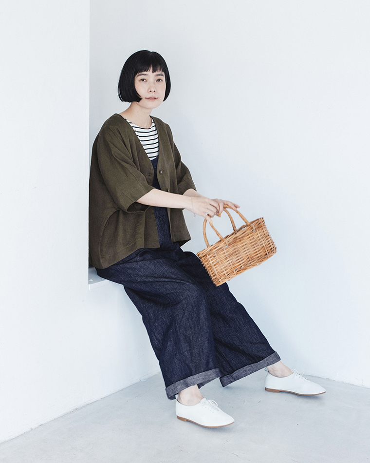 カーキのリネンジャケットをボーダートップスとダークデニムに合わせ、かごバッグを持って腰掛けた着用コーディネート画像