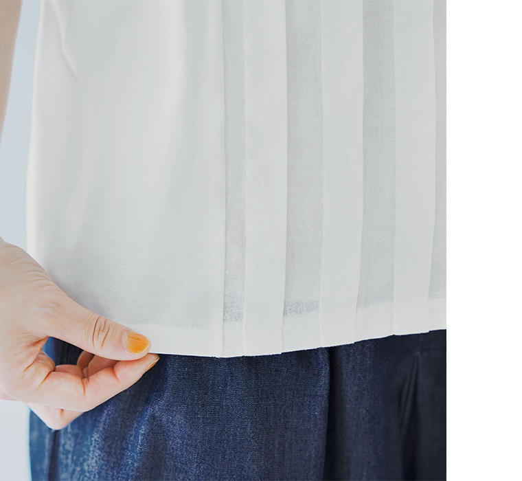 オフホワイトのトップスの裾を手で軽く持ち上げて質感を見せたディテール画像