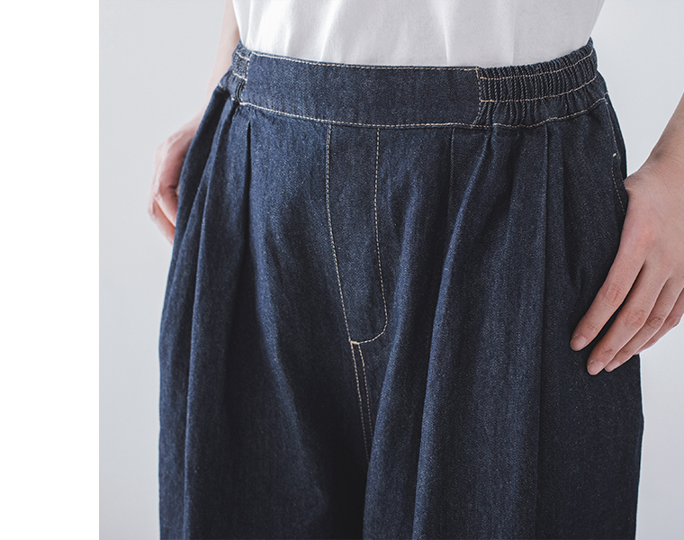 インディゴデニムのウエストまわりのステッチとタックを写した着用ディテール画像（白トップス合わせ）