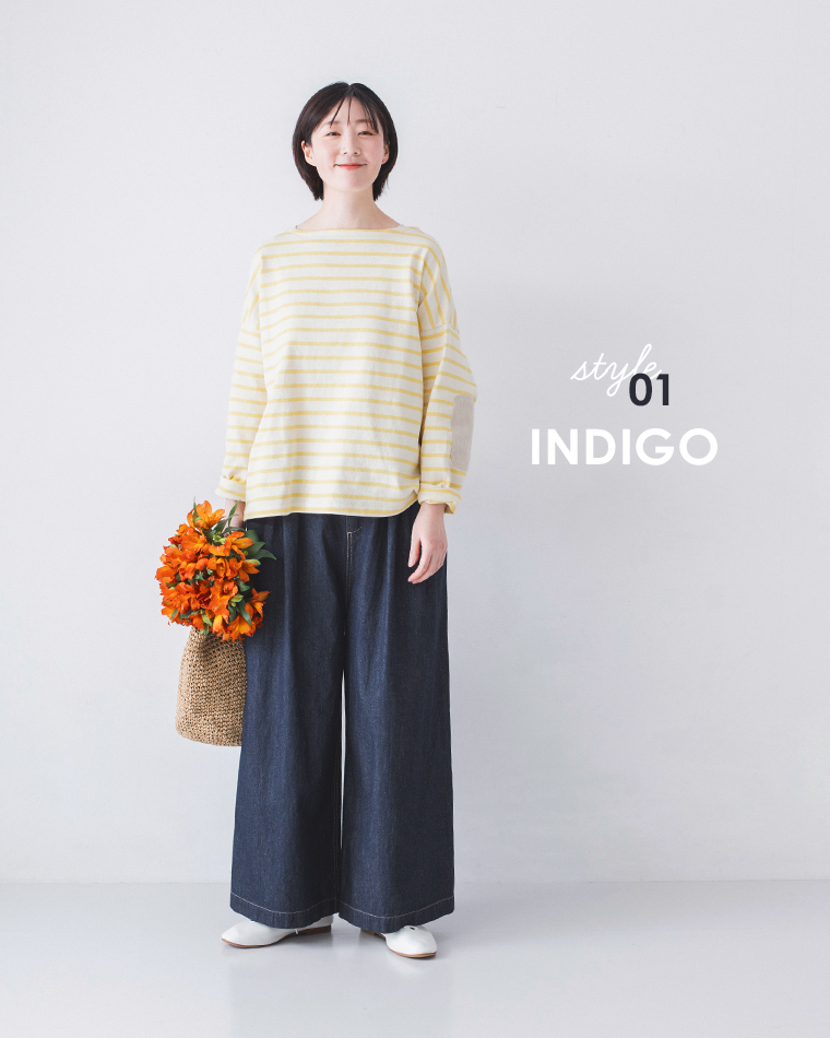 イエロー×ホワイトのボーダートップスにインディゴのワイドデニムパンツと白シューズを合わせ、花入りのかごバッグを持つ着用コーディネート画像