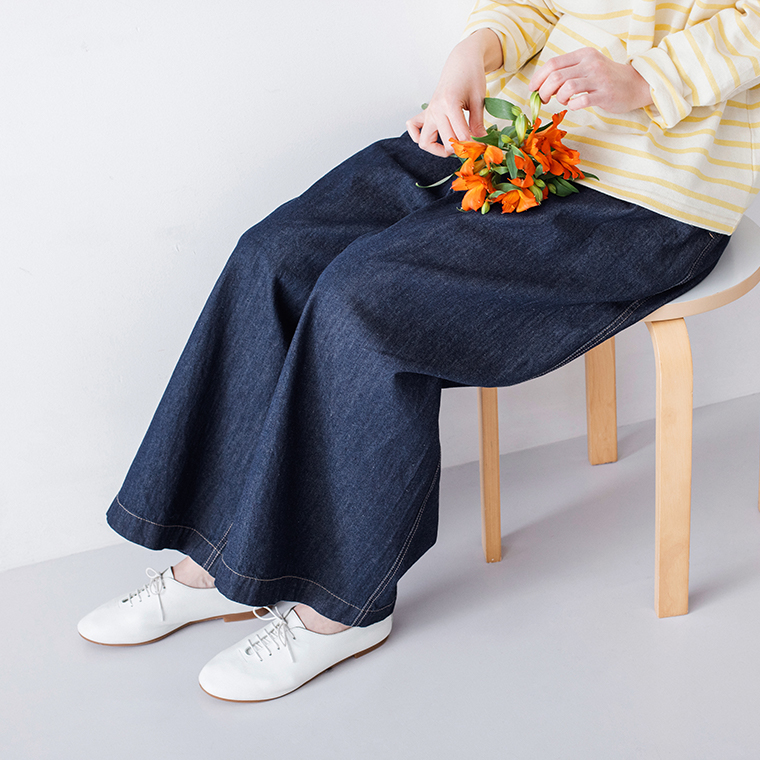 イエロー×ホワイトのボーダートップスにインディゴのワイドデニムパンツと白シューズを合わせ、花を手に持って椅子に座る着用コーディネート画像