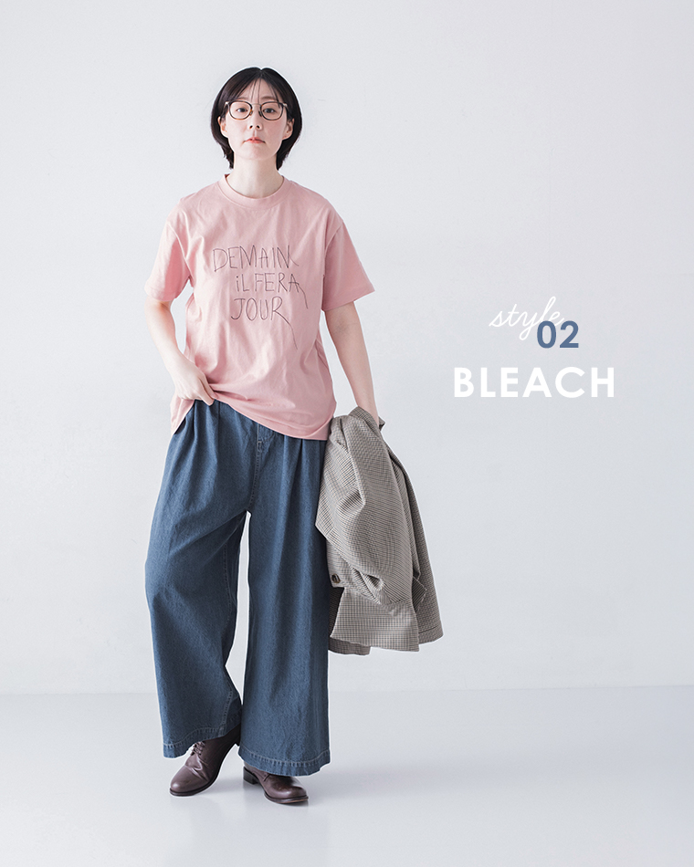 ピンクのロゴTシャツにブリーチデニムパンツとブラウンシューズを合わせ、ジャケットを手に持つ着用コーディネート画像