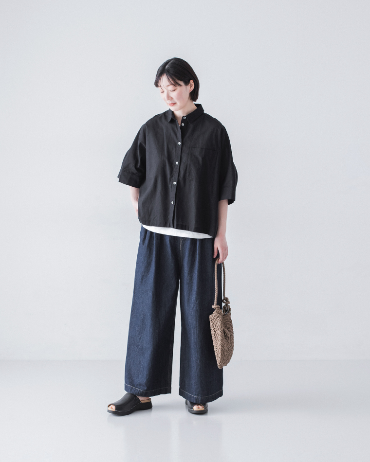 黒のボタンシャツにインディゴのワイドデニムパンツと黒サンダルを合わせ、かごバッグを手に持つ着用コーディネート画像