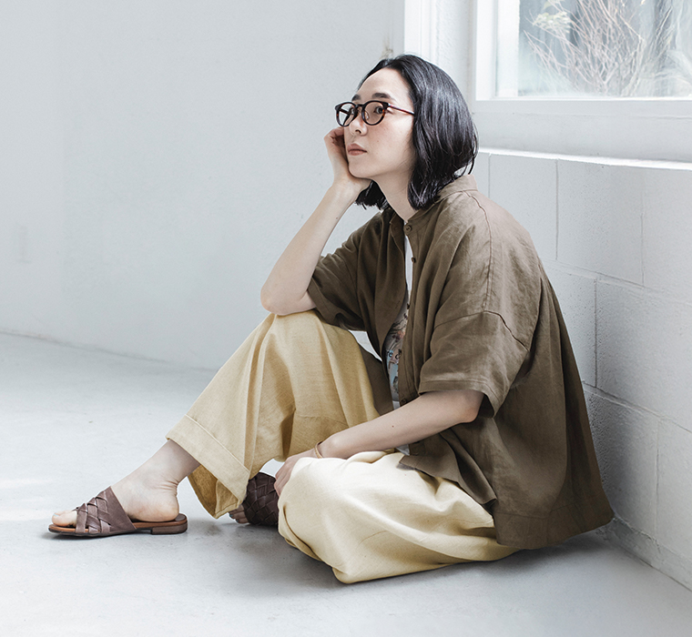 100%リネンちび襟シャツブラウンを着たモデルが座って横向きで壁にもたれている