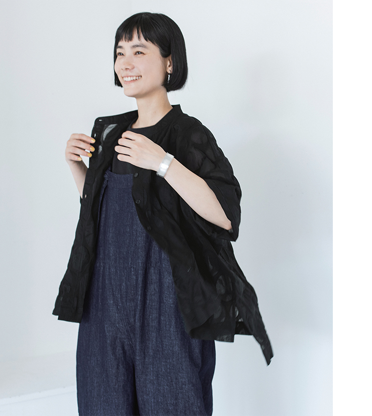 ブラックのシアーシャツをサロペットの上に羽織った人物の上半身カット