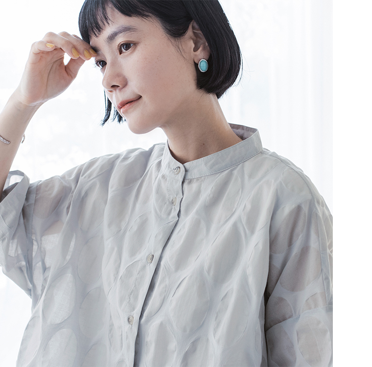 ライトグレーのシアートップスを着た人物の上半身アップ（楕円ドット柄の透け感と軽やかな質感が見えるカット）