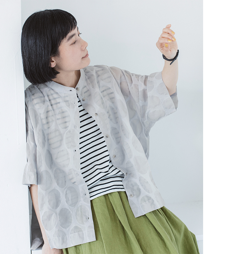 ライトグレーのシアートップスにボーダーとグリーンスカートを合わせた人物の上半身カット