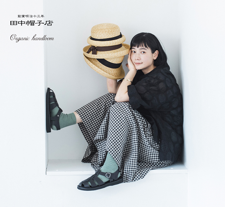 田中帽子店／Organic handloom 麦わら帽子を手に座ってレザーサンダルを履いているカット