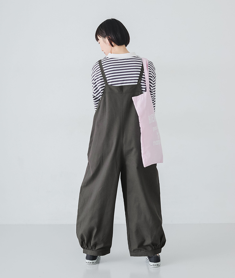 ごきげんになれるサロペットを着たモデルが後ろ向きで立っている