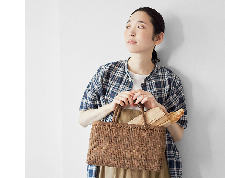 白皮あじろ編みの横長カゴバッグにパンを入れて持つ女性モデルの上半身