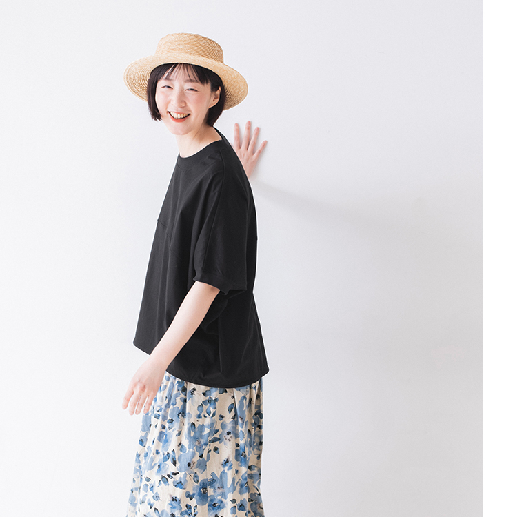 &yarn ポンチョプルオーバー（ブラック）を着用した人物の横向きカット — 青系花柄スカートと麦わら帽子を合わせた軽やかな夏のスタイリング