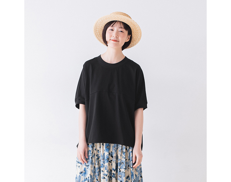 &yarn ポンチョプルオーバー（ブラック）を着用した人物の正面カット — 青系花柄スカートと麦わら帽子を合わせた軽やかな夏のスタイリング