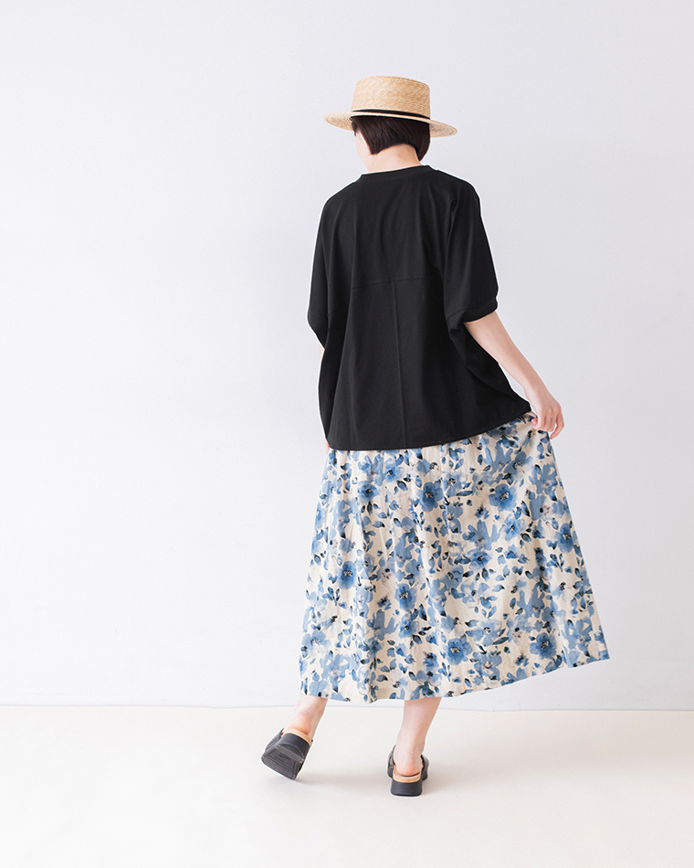 &yarn ポンチョプルオーバー（ブラック）を着用した人物の後ろ姿 — 青系花柄スカートと麦わら帽子を合わせた軽やかな夏のスタイリング
