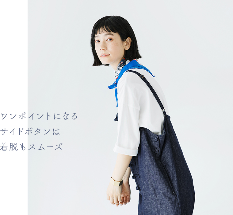 Dgy コットンリネンデニムチャイナボタンサロペットを白シャツに重ねた横向きコーディネート（サイドボタンが見えるデザイン。「ワンポイントになるサイドボタンは着脱もスムーズ