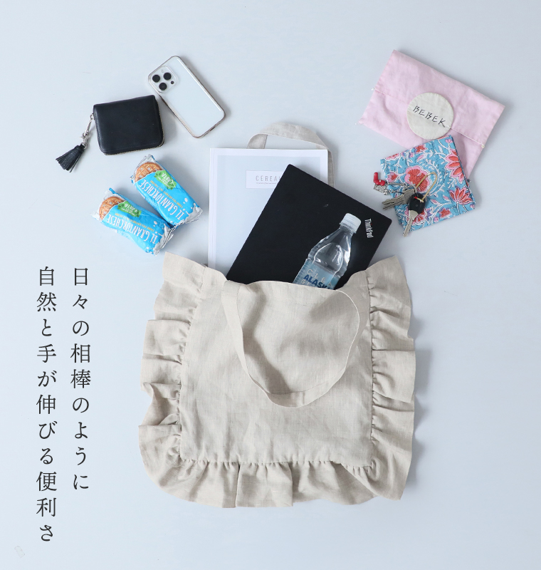 08Mabの リネンフリルトートバッグ（キナリ）の使用イメージ。スマートフォンや財布、ノート、水筒など日常の持ち物を入れた様子。画像内テキスト「日々の相棒のように 自然と手が伸びる便利さ」。