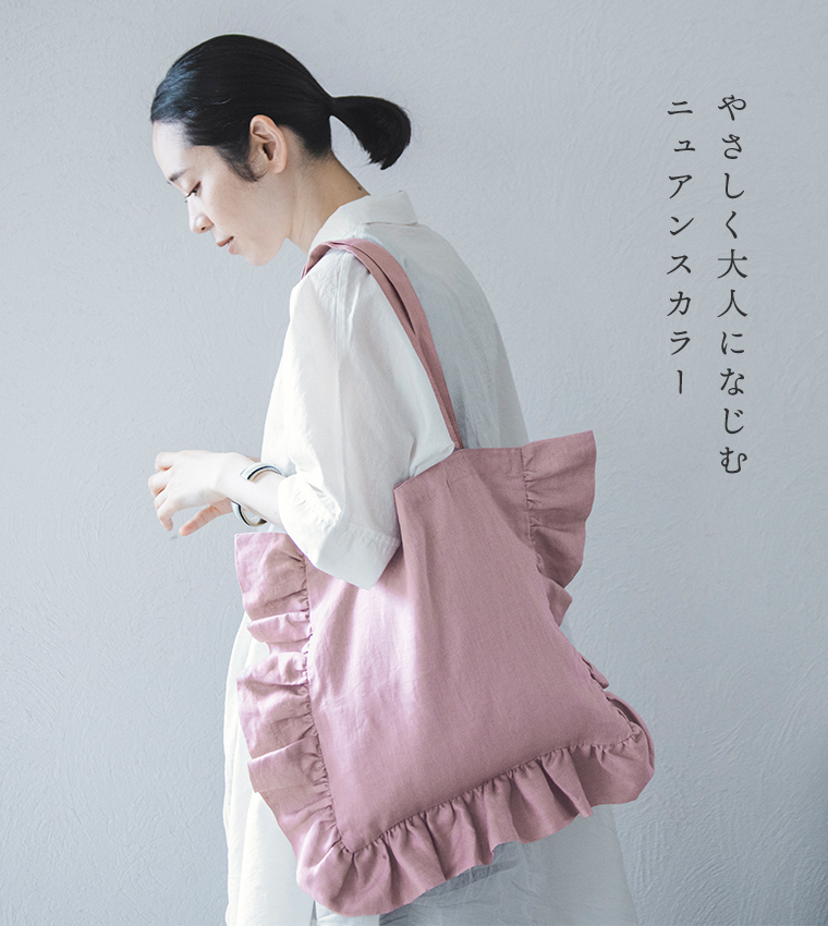 08Mabの リネンフリルトートバッグ（ダスティーピンク）を椅子に掛けたコーディネート画像。白のロングシャツワンピースにワイドパンツを合わせた女性が窓辺で座る姿。画像内テキスト「やさしく大人になじむ ニュアンスカラー」。