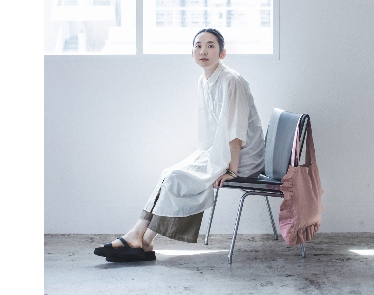 08Mabの リネンフリルトートバッグ（ダスティーピンク）を肩に掛けた女性のコーディネート画像。白のロングシャツワンピースにワイドパンツを合わせ、柔らかな光に包まれたナチュラルな雰囲気。