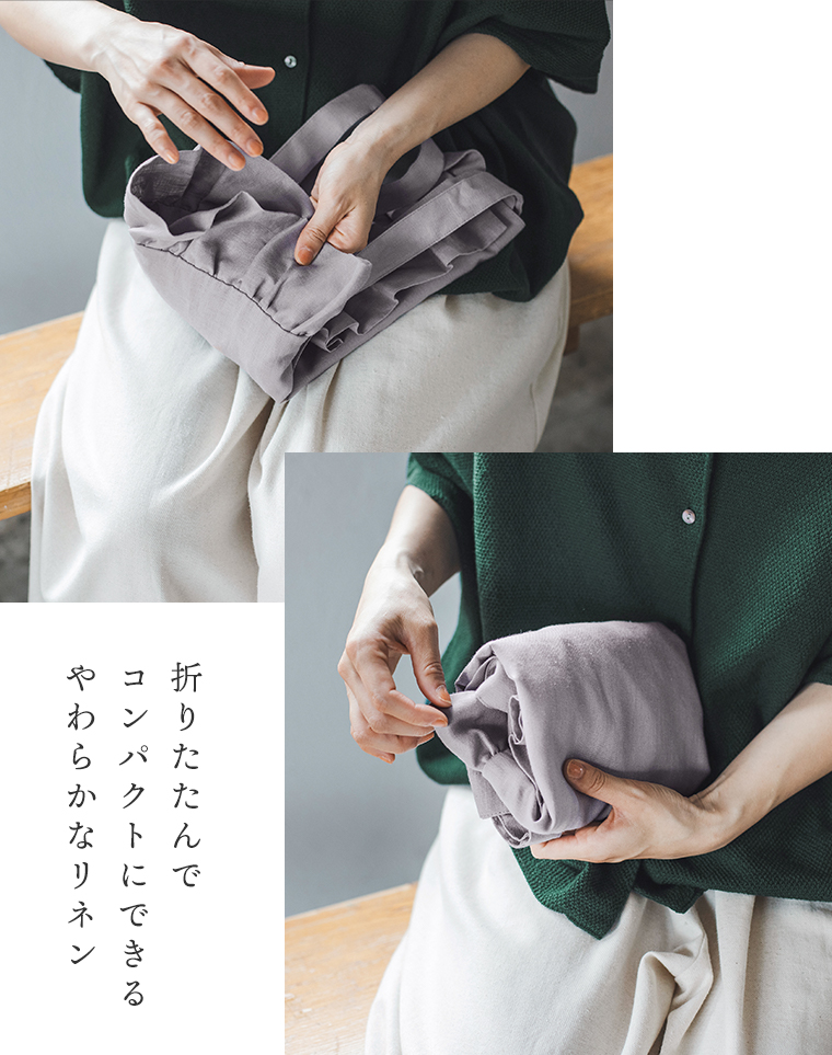08Mabの リネンフリルトートバッグ（スチールグレー）を折りたたむ様子。グリーンのトップスに白のパンツを合わせた女性が、柔らかなリネン素材のバッグをコンパクトにまとめている手元のアップ。画像内テキスト「折りたたんで コンパクトにできる やわらかなリネン素材」。
