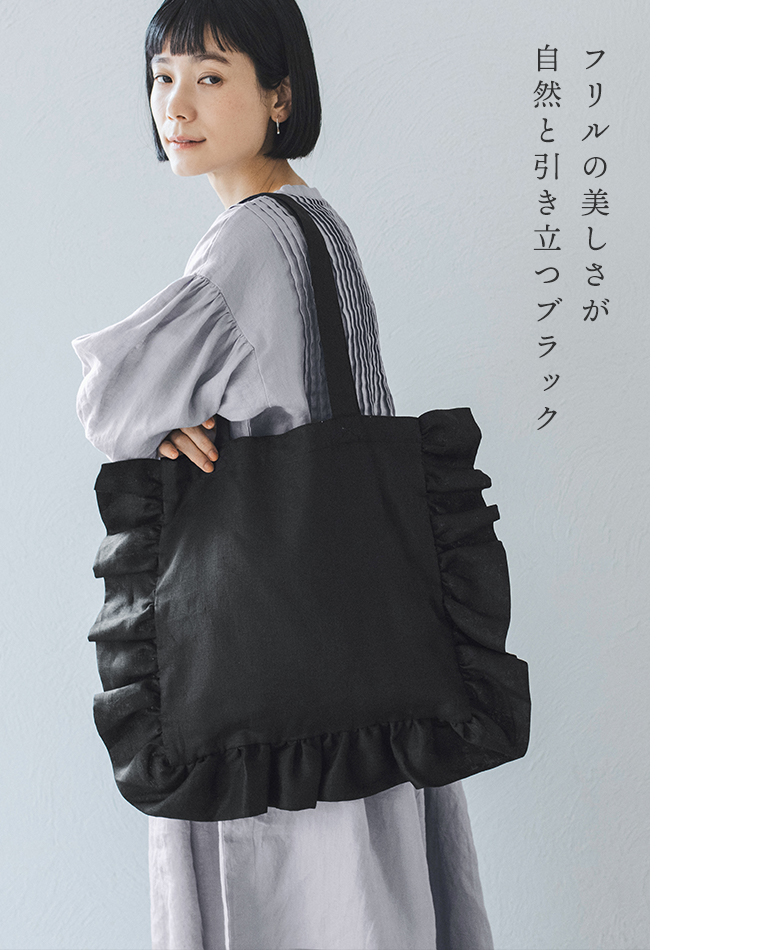 08Mabの リネンフリルトートバッグ（ブラック）を肩に掛けた女性のコーディネート画像。ライトグレーのピンタックワンピースに合わせ、フリルの美しさが際立つシックな印象。画像内テキスト「フリルの美しさが 自然と引き立つブラック」。